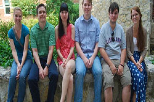 Six students sitting on ledge with garden in background