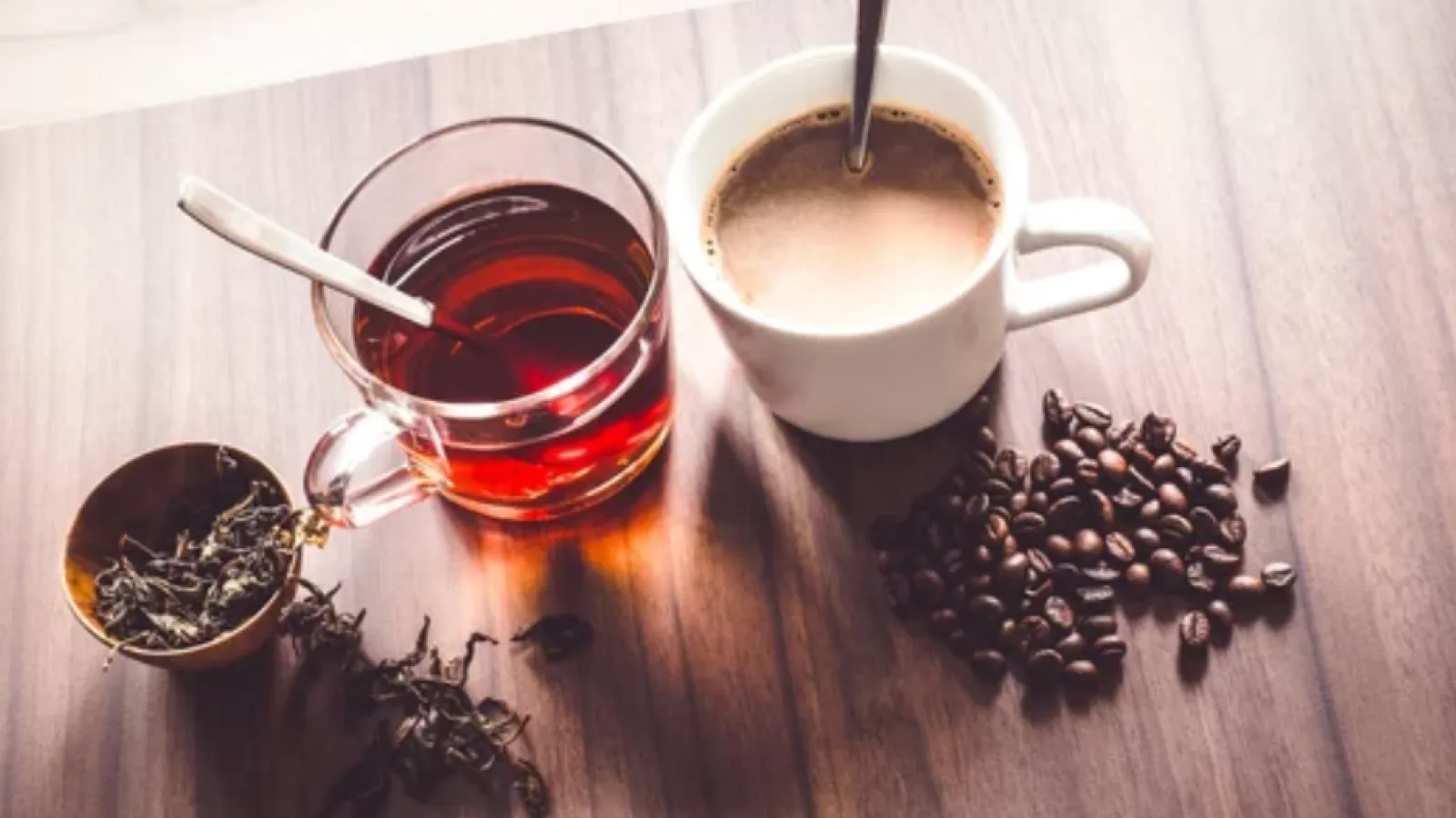 a cup of tea and a cup of coffee surrounded by tea leaves and whole coffee beans