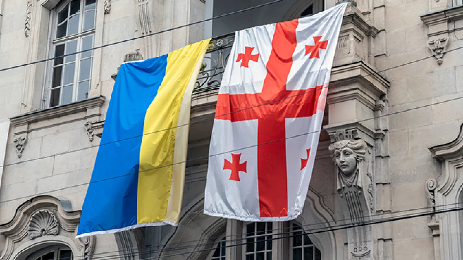 The Ukrainian flag )left) and Georgian flag (right) hang next to each other on the side of a building. 