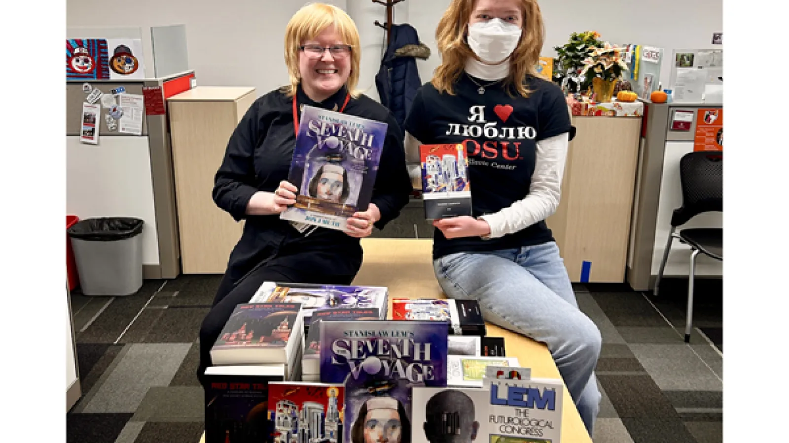 Alicia Baca (CSEEES outreach coordinator) and Sophie Papp (CSEEES intern) sitting on a table with stacks of Slavic science fiction books.