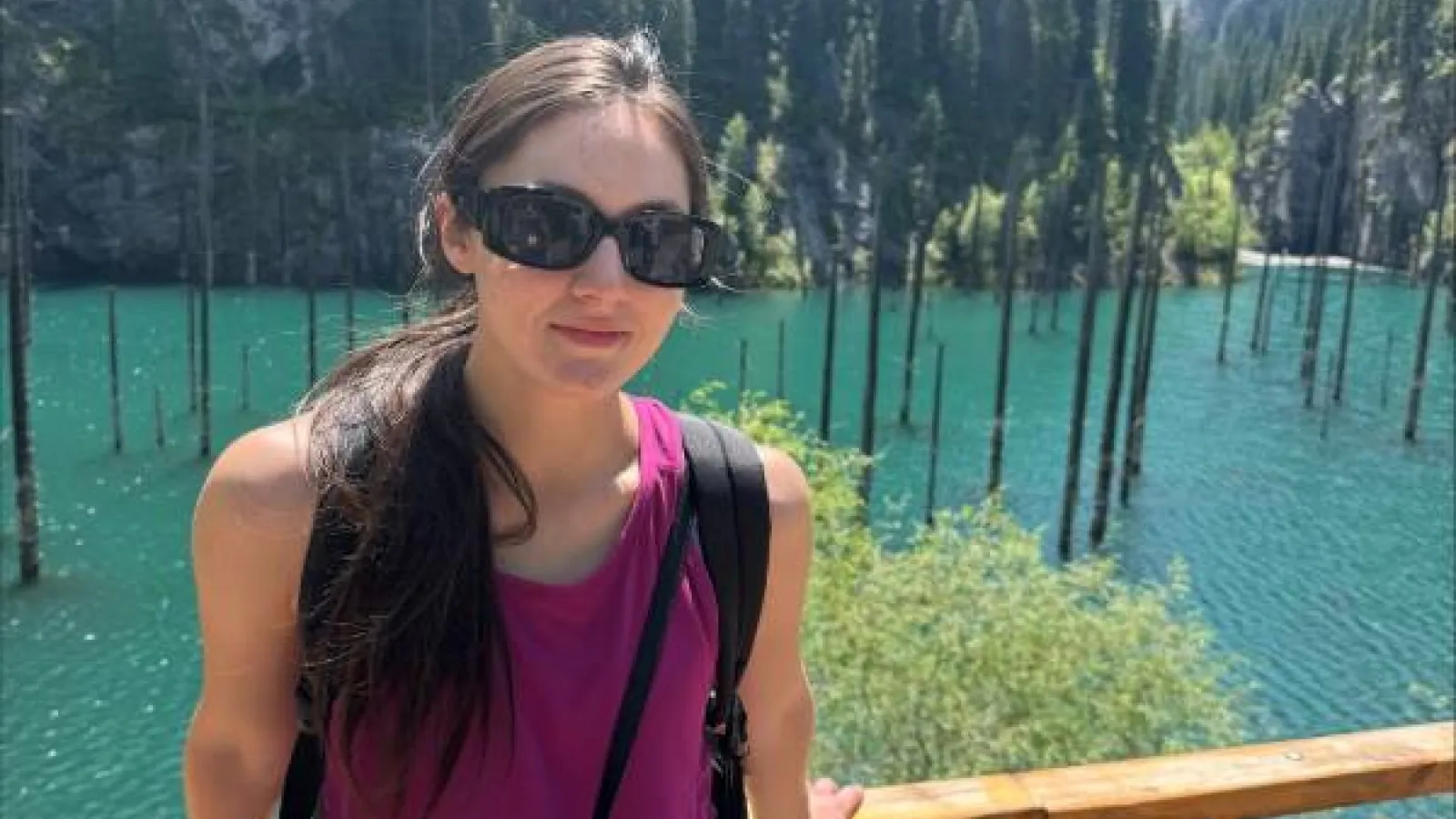 Sophie Boelk stands in front of a mountainous landscape with turquouise water and submerged tree trunks