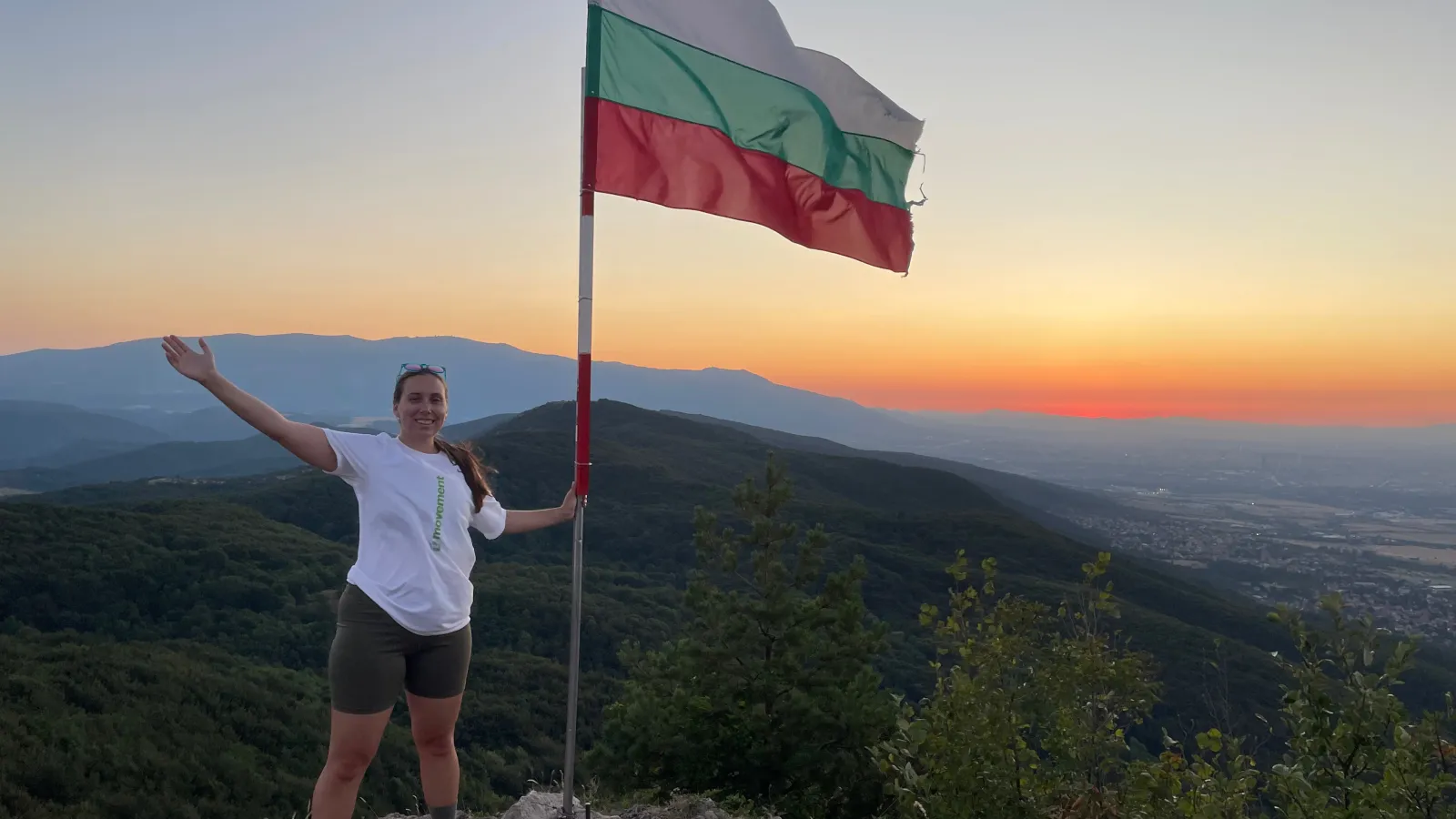 Siobhan standing next to the Bulgarian flag on top of a mountain. 