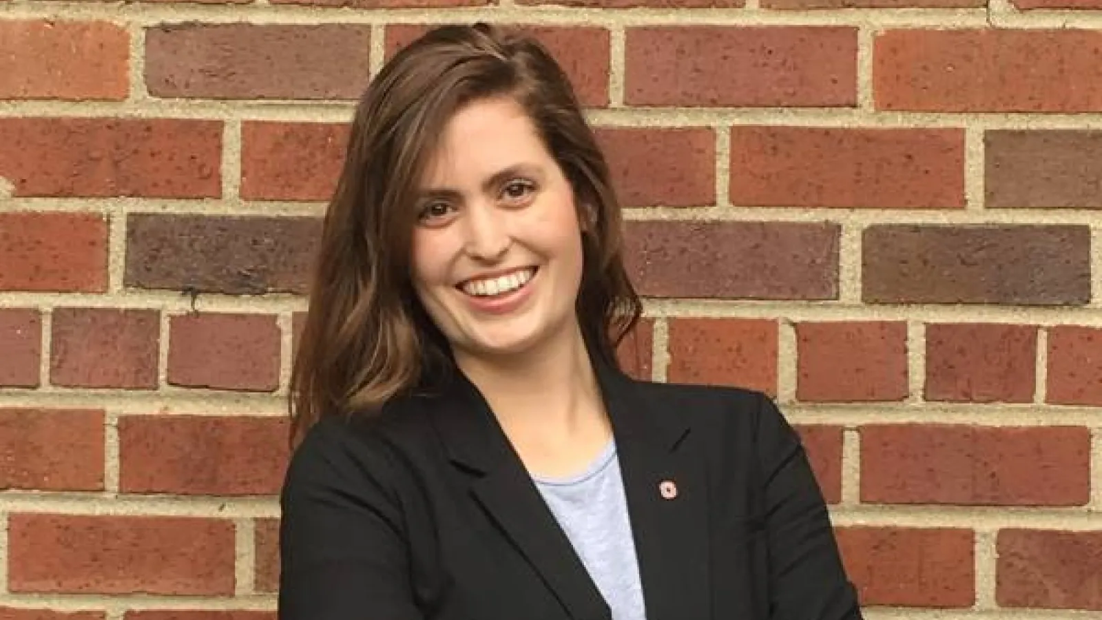 A portrait of Katie McAfee standing in front of a brick wall