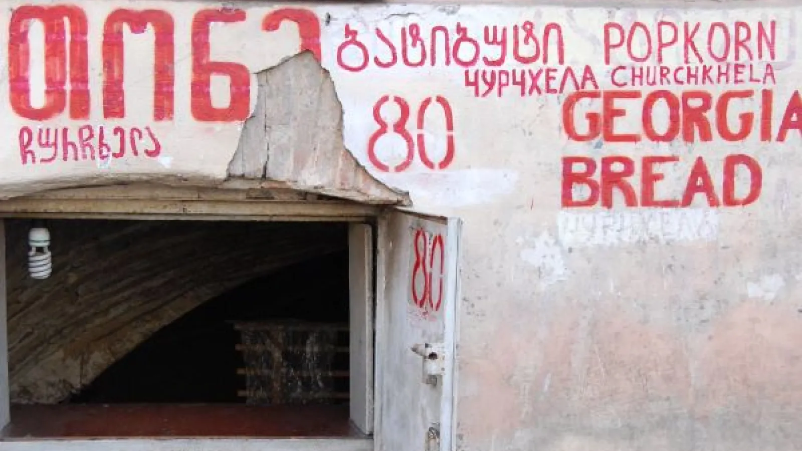 A window in a stuccoed wall with the words popkorn, churchkhela and Georgian bread written above in Georgian, English and Russian