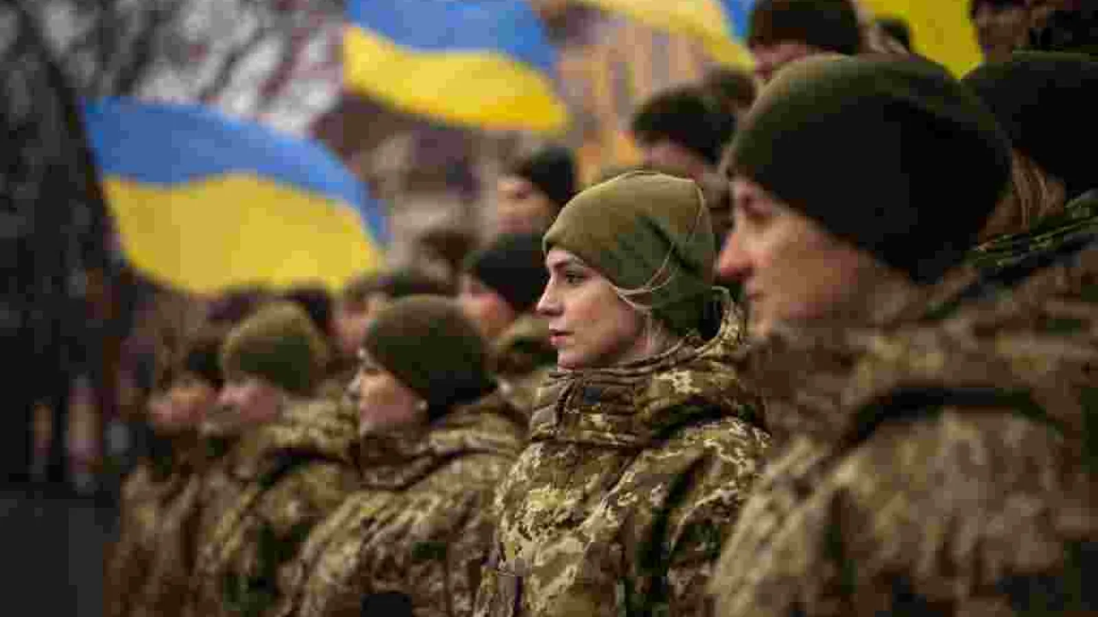 Female Ukrainian solders standing next to the Ukrainian flag