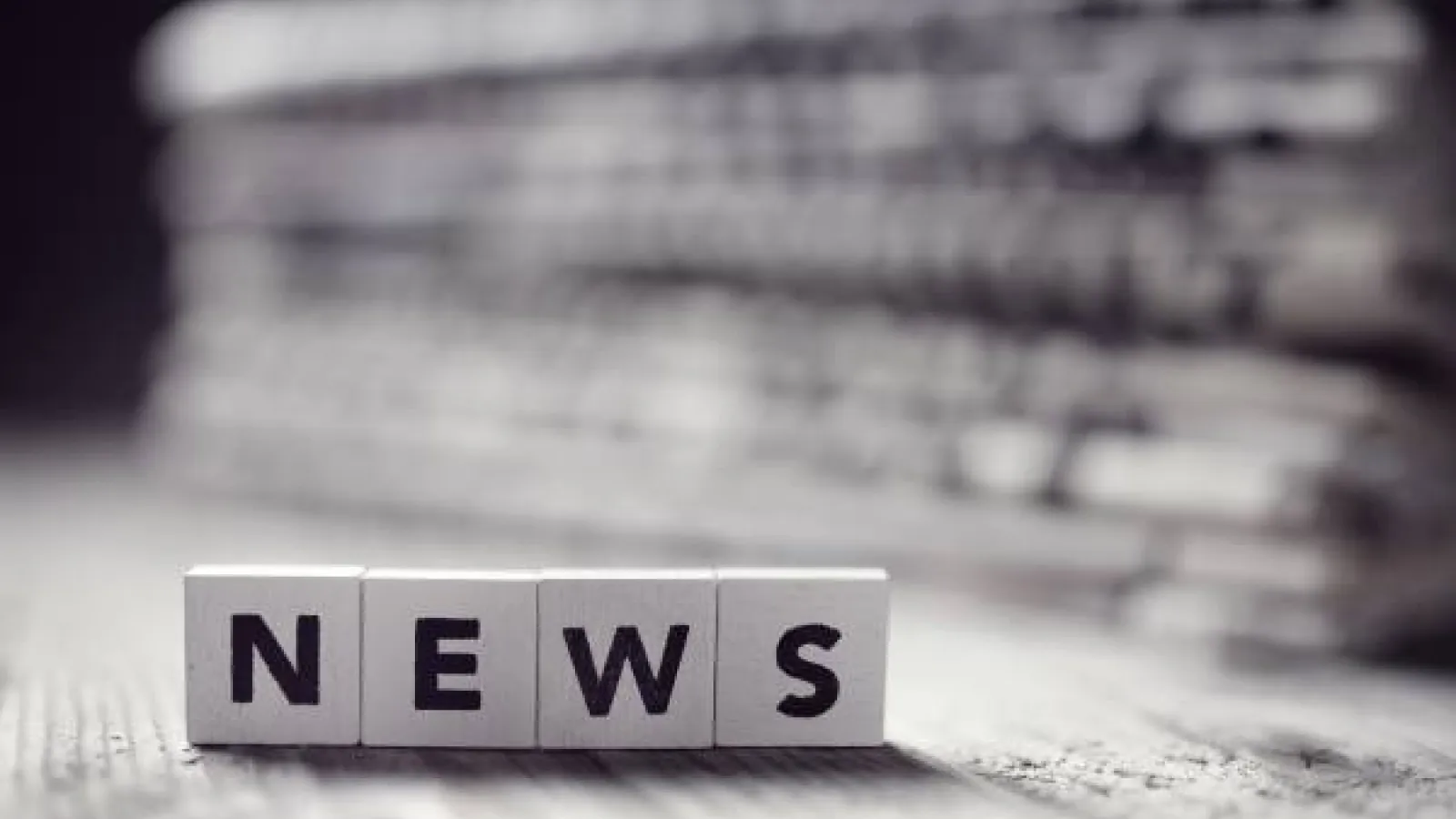 Alphabet blocks form the word "news" in front of a stack of newspapers