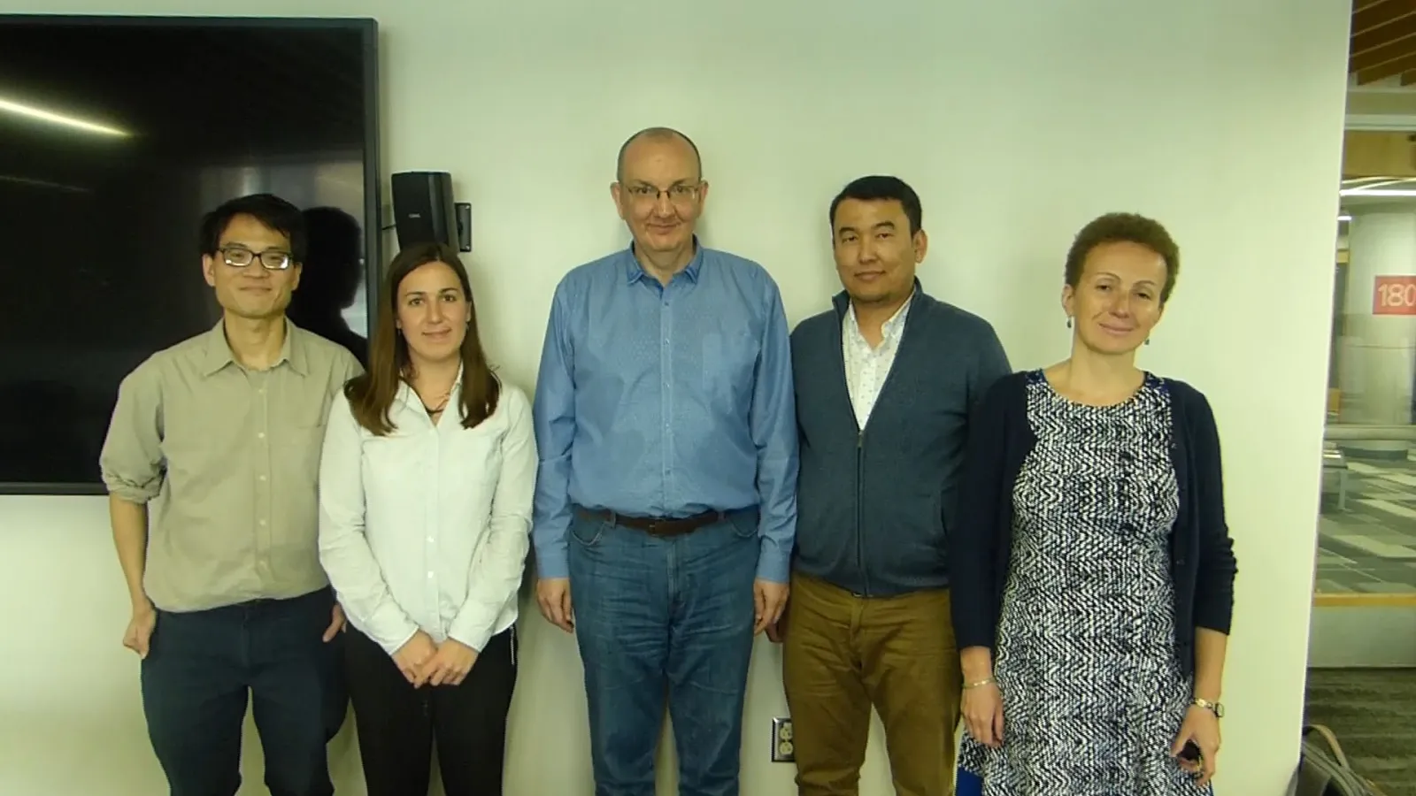 5 people standing against a wall smiling at the camera