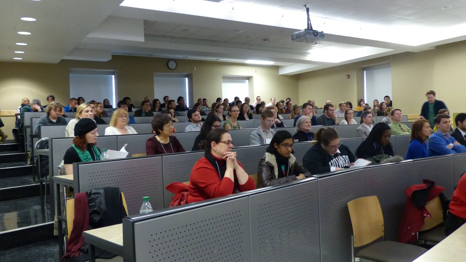 Large crowd of people seated in rows at long seminar tables