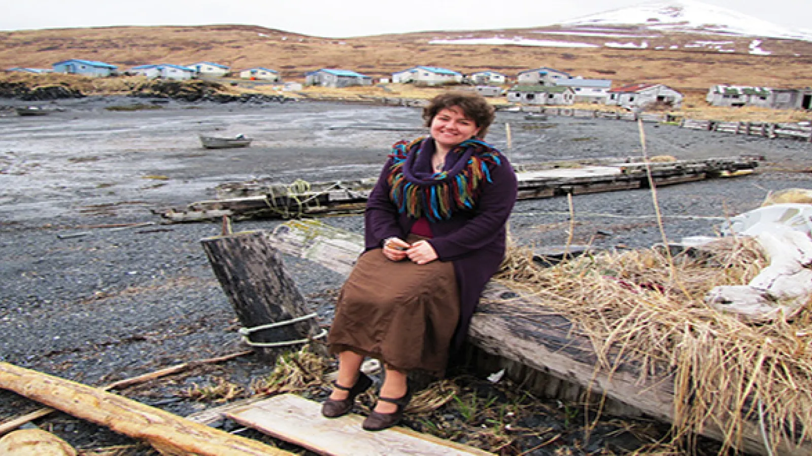 Woman sitting on a piece of timber with a village and mountains far away in background