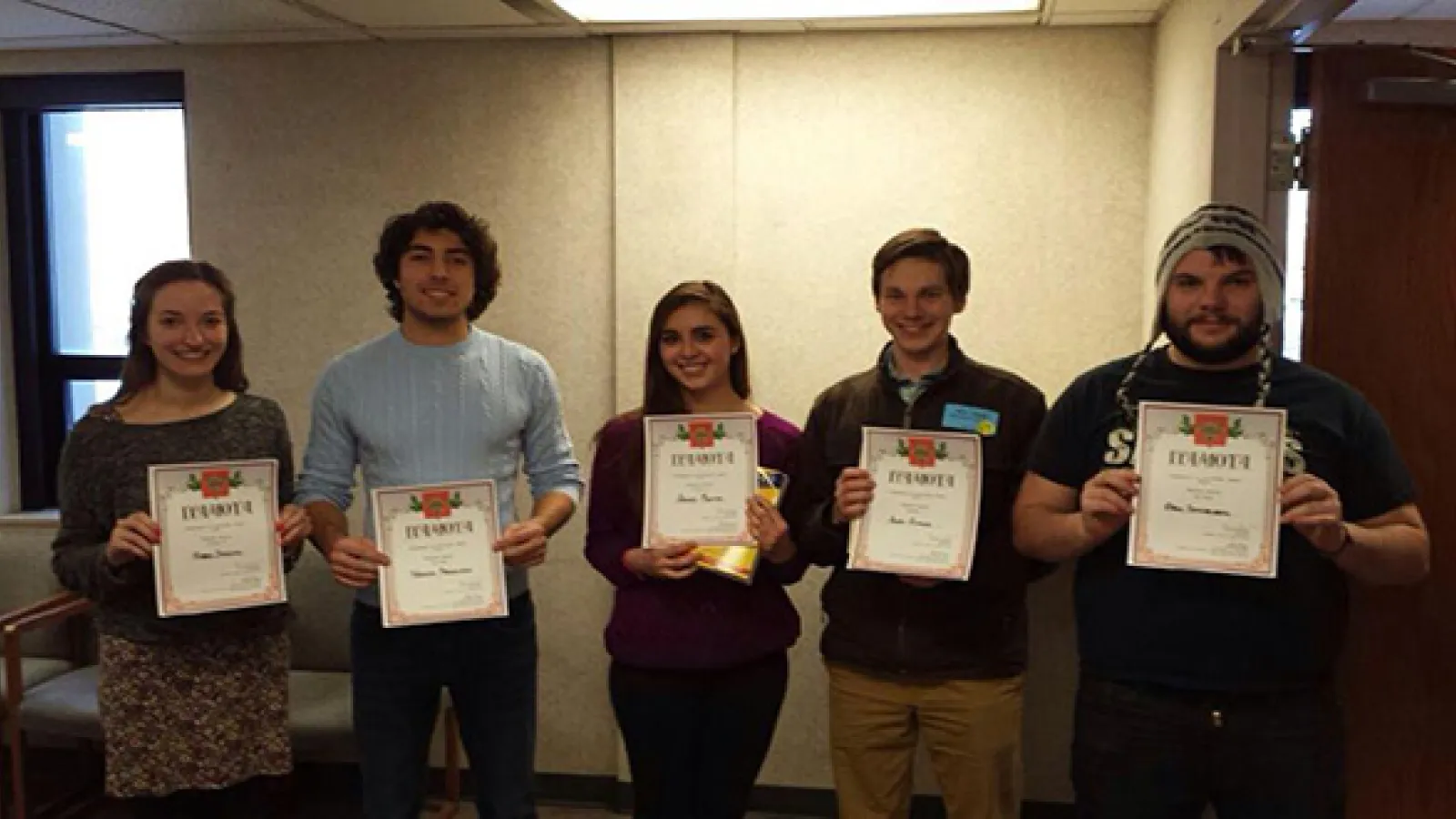 Five students standing in row each holding a certificate