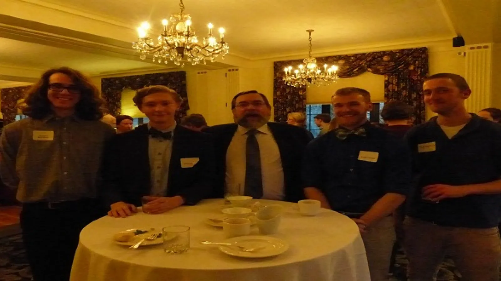Group of six men standing shoulder to shoulder in a larger room by a table