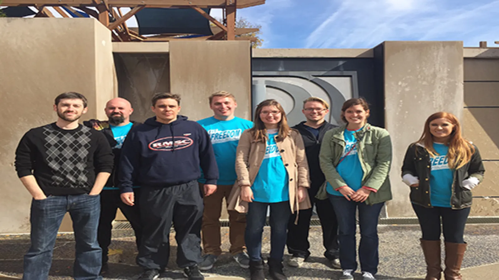 8 students standing in two loose rows facing the camera in front of a building
