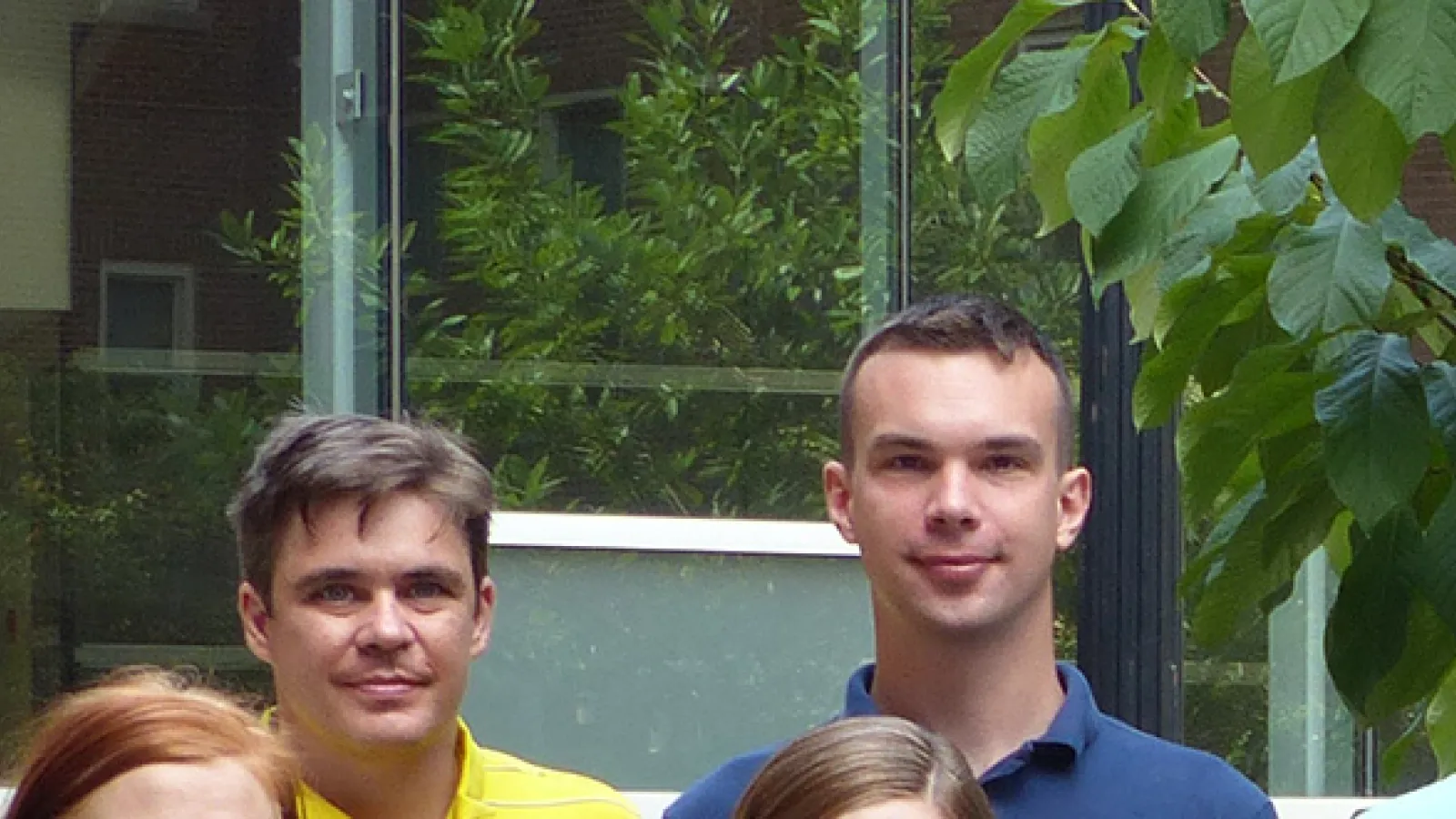 Photo of two men's faces from a distance with a window and greenery in the background