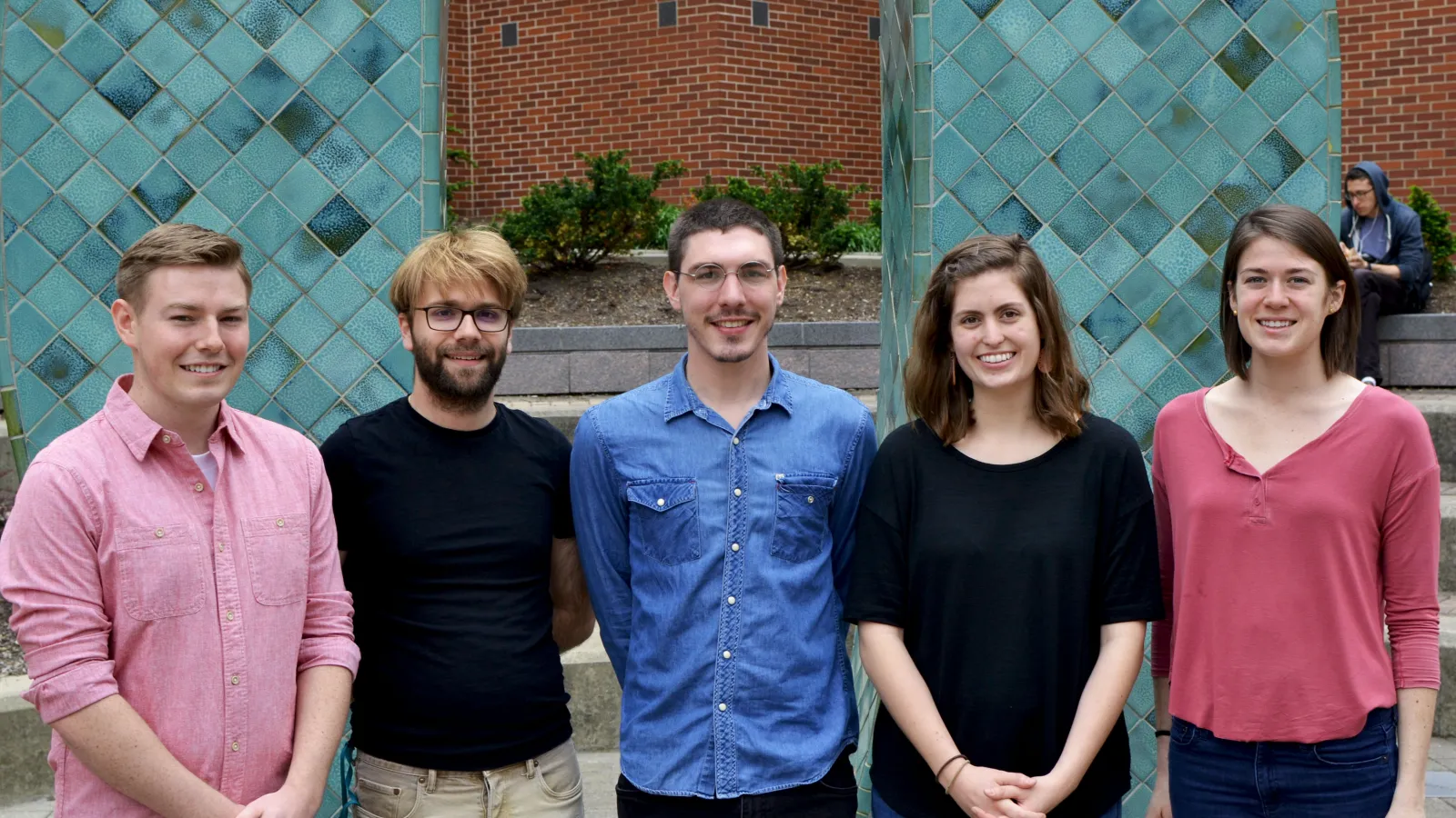 5 people standing shoulder-to-shoulder with a large blue tile background.