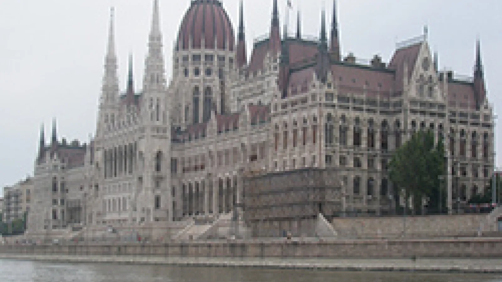 Long Gothic building with red tile roof on the banks of a river