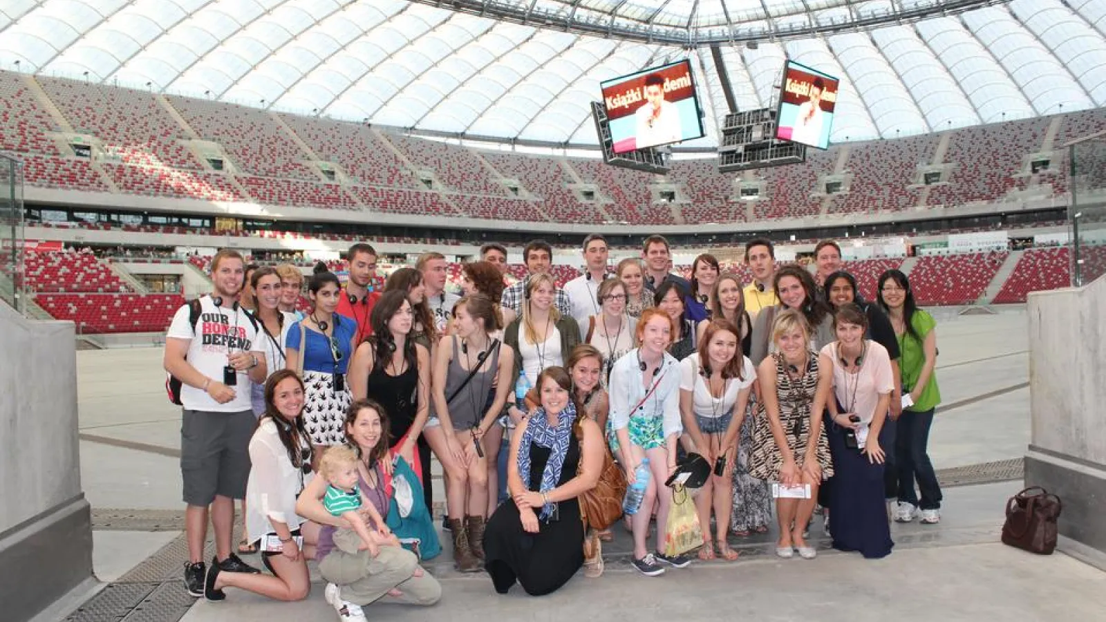Large group of people standing between the stands in a stadium in rows next to each other