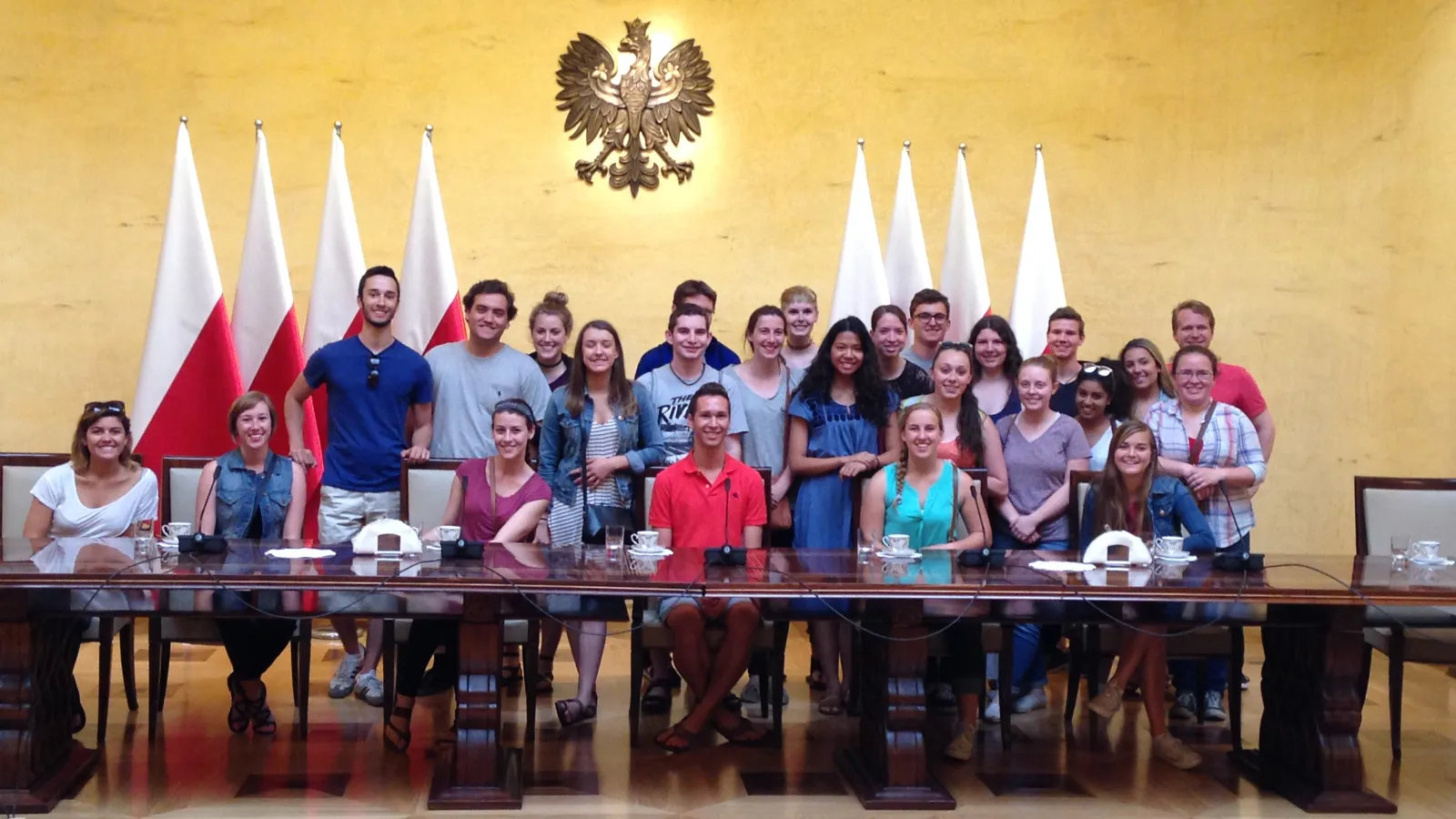 Two rows of students sitting underneath Polish government seal