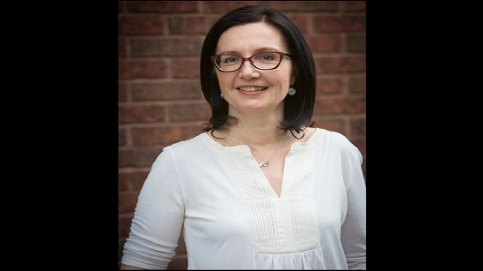 A woman with dark hair and glasses looking at the camera