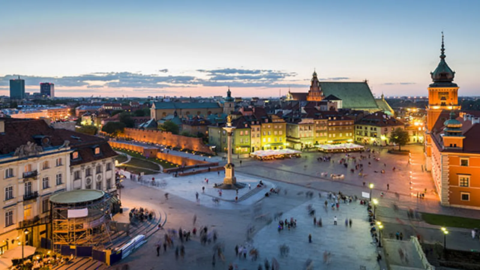 Image of a city taken from above in the evening, showing a square, brick buildings, and illuminated lights