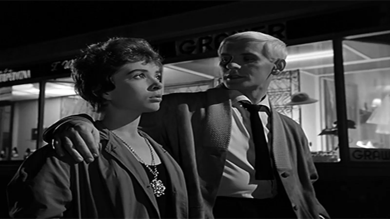Black and white photo of man and woman walking down street with man's arm around woman's shoulders