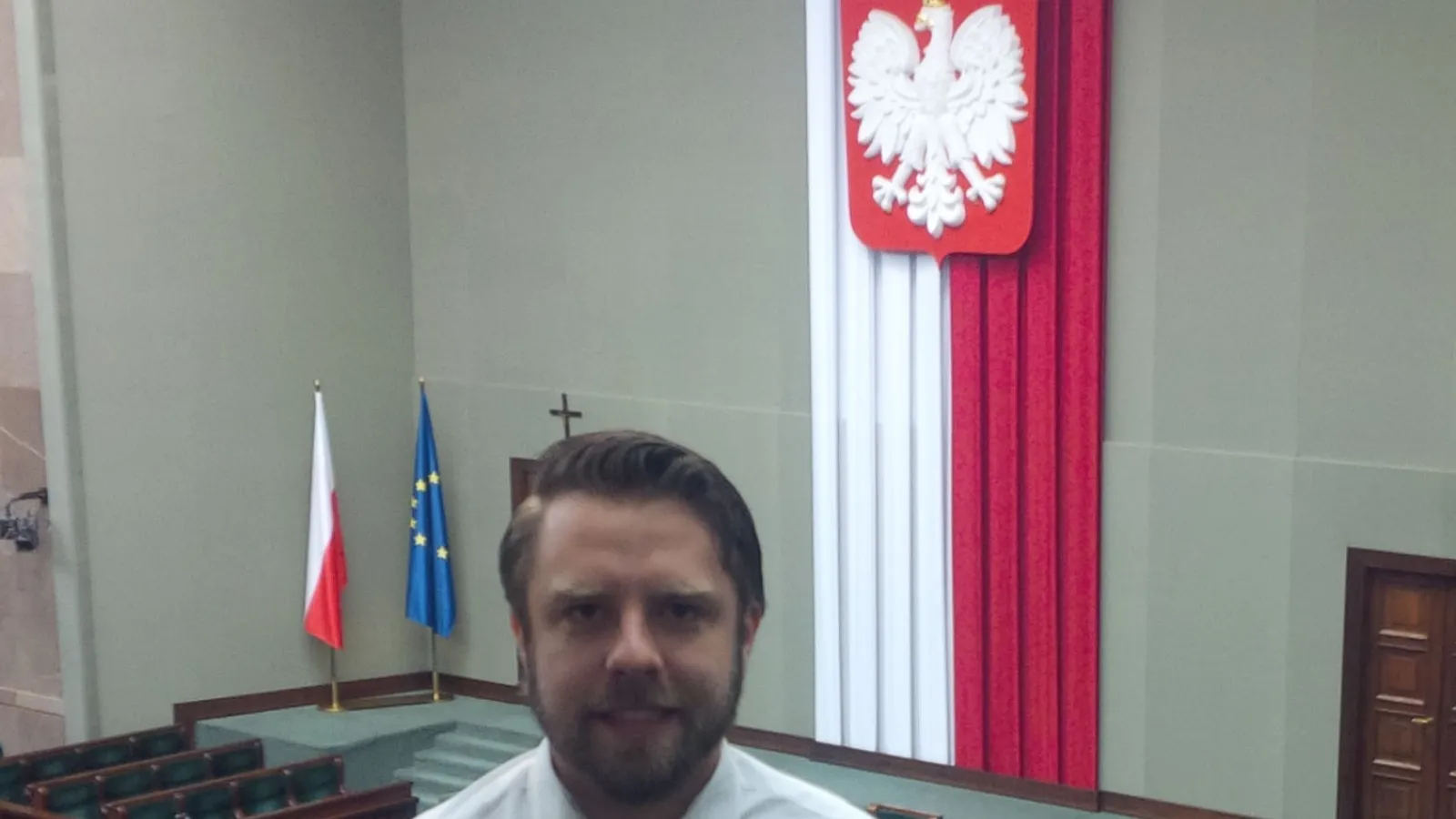 A man standing overlooking a gallery with a flag hanging in background.
