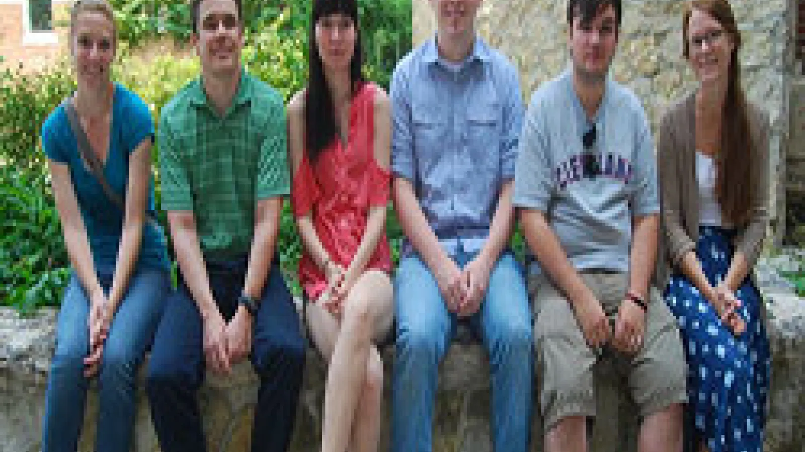 Six students sitting on ledge with garden in background