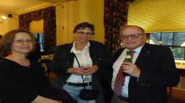 Two women and a man standing next to each other with drinks in their hand in a reception room