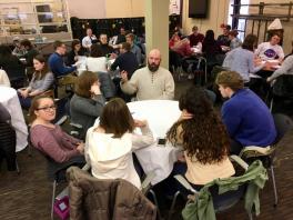 Students sitting at a round table listening to a man speak
