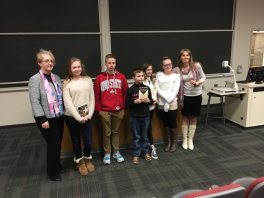 7 people standing and smiling in front of room, two holding up book prizes