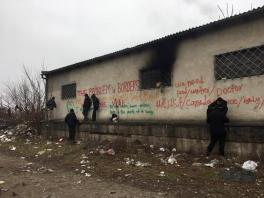 "The Problem is Borders" and several other says spray painted on an abandoned building with several men hanging around its exterior
