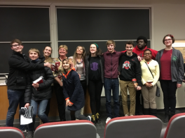 Students smiling and standing next to each other in the front of a classroom