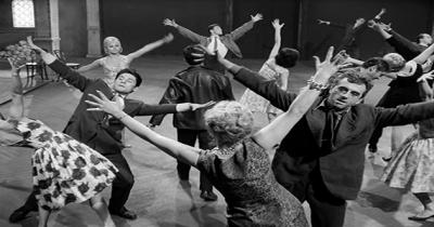 A large group of people dancing in a hall with their hands in the air