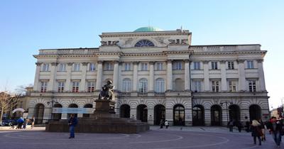 Large grey three story building with columns, square in front