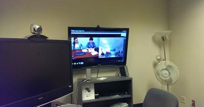 Monitor Showing Both Sides of Distance Lecture Large TV screen hanging from wall with two images split on screen
