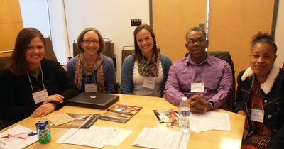 4 women and 1 man sit at a table shoulder-to-shoulder