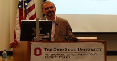 Professor Viacheslav Morozov Man standing at a podium speaking with an American flag behind him