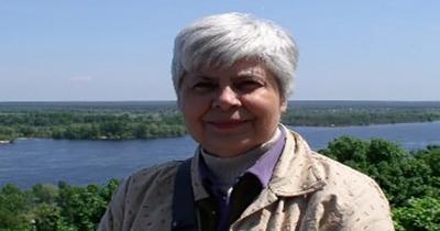 Photo of a woman's upper torso and face with a river and trees in the background