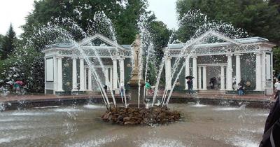 Large fountain with statue in center spraying water into air with arches in the background