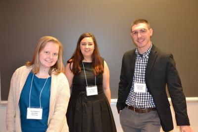 2017 Panelists Ana Kabakova, Joanna Kaganovich, and Randall Rowe Two women and a man standing by each other smiling in front of a black chalkboard