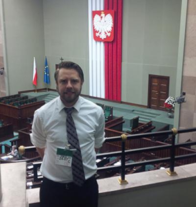 Man standing on a balcony in a large room with the Polish flag hanging in background
