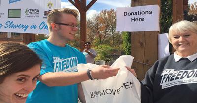 CSEES MA Students Katie McAfee and Jon Harris at the Fit for Freedom 5K A woman's face and a man standing holding a white plastic bag at a race checkpoint