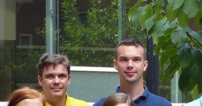 Photo of two men's faces from a distance with a window and greenery in the background