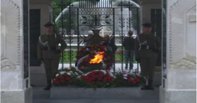 Tomb of the Unknown Solider in Warsaw, Poland Two soldiers in uniform standing guard on either side on a stone monument with a flame and surrounded by bouquets