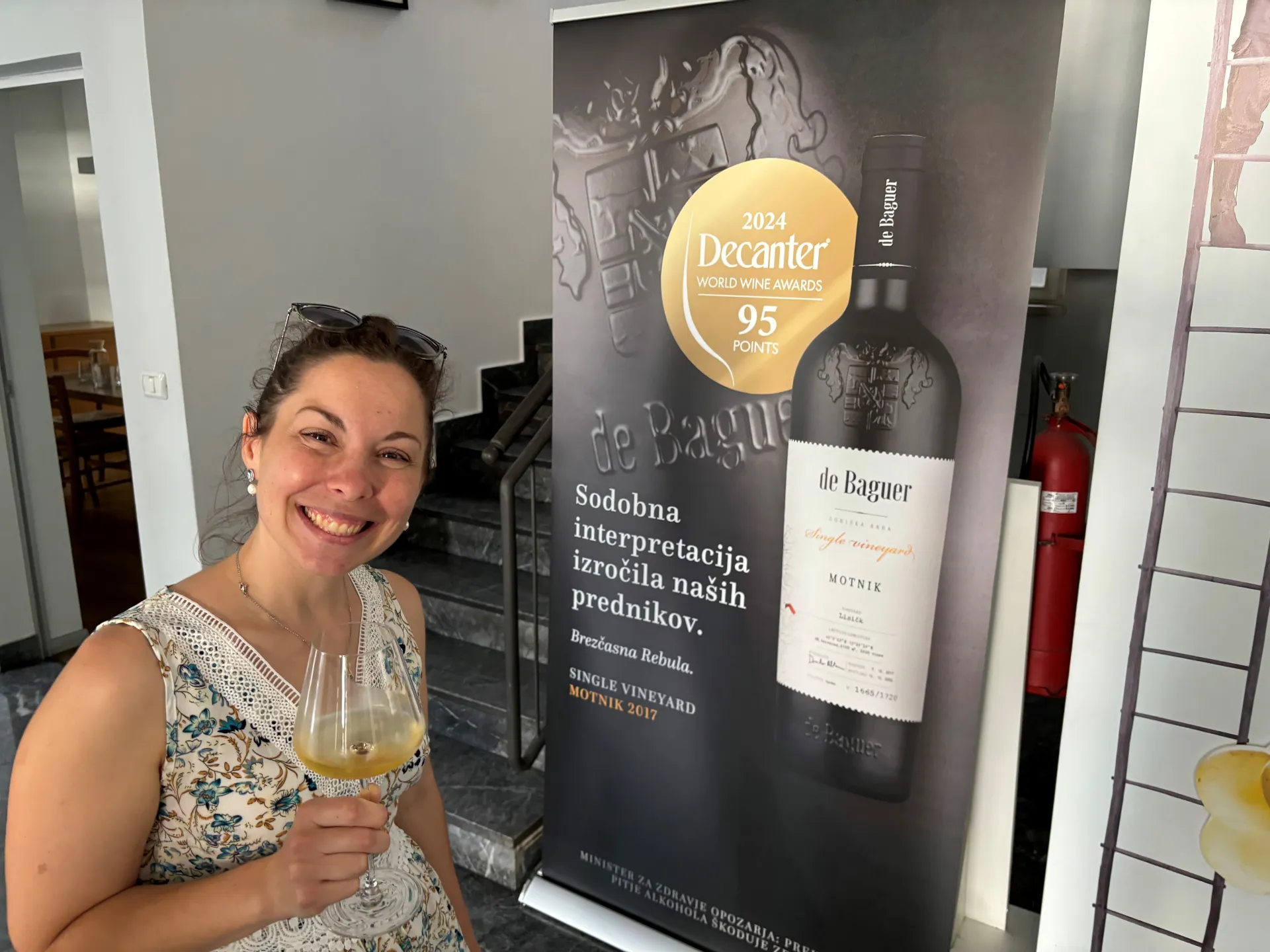 Dr. Mariana Grohar enjoying sparkling wine while standing next to the poster of an award winning wine.