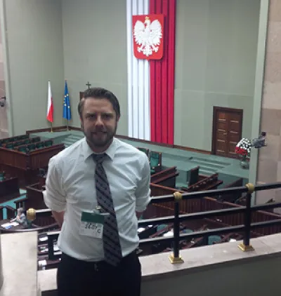 Man standing on a balcony in a large room with the Polish flag hanging in background
