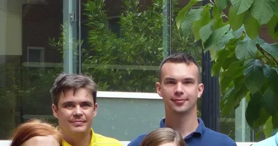 Photo of two men's faces from a distance with a window and greenery in the background
