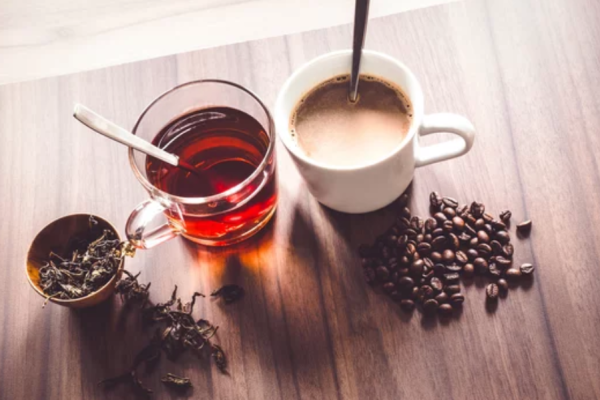 a cup of tea and a cup of coffee surrounded by tea leaves and whole coffee beans