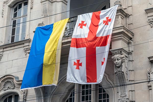 The Ukrainian flag )left) and Georgian flag (right) hang next to each other on the side of a building. 