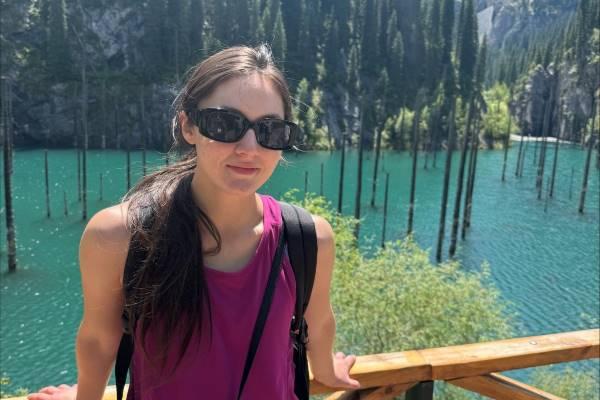 Sophie Boelk stands in front of a mountainous landscape with turquouise water and submerged tree trunks