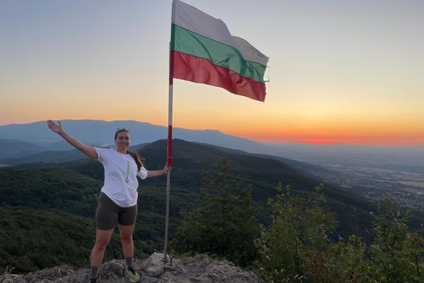 Siobhan standing next to the Bulgarian flag on top of a mountain.